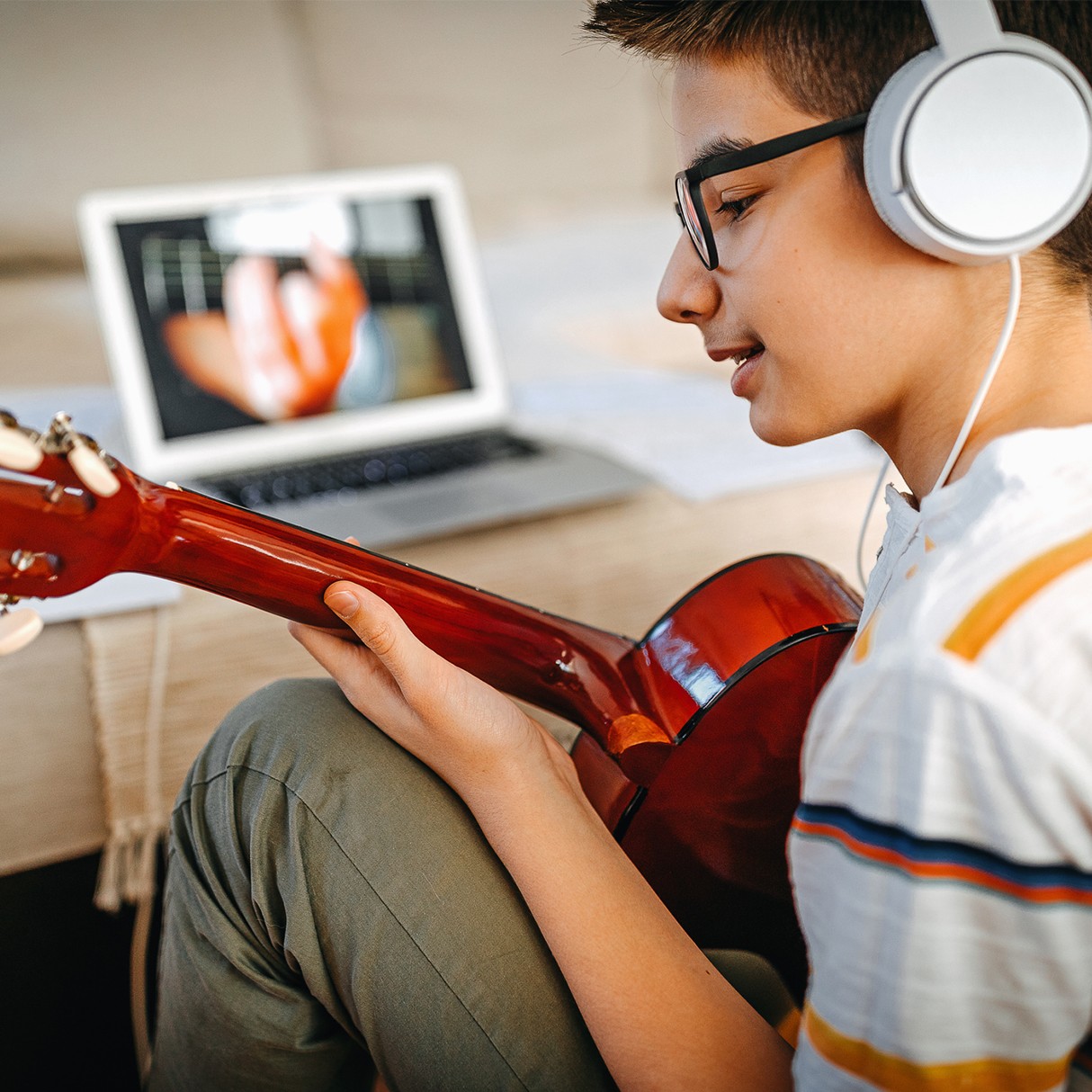 Male student learning guitar on a video chat with his teacher.